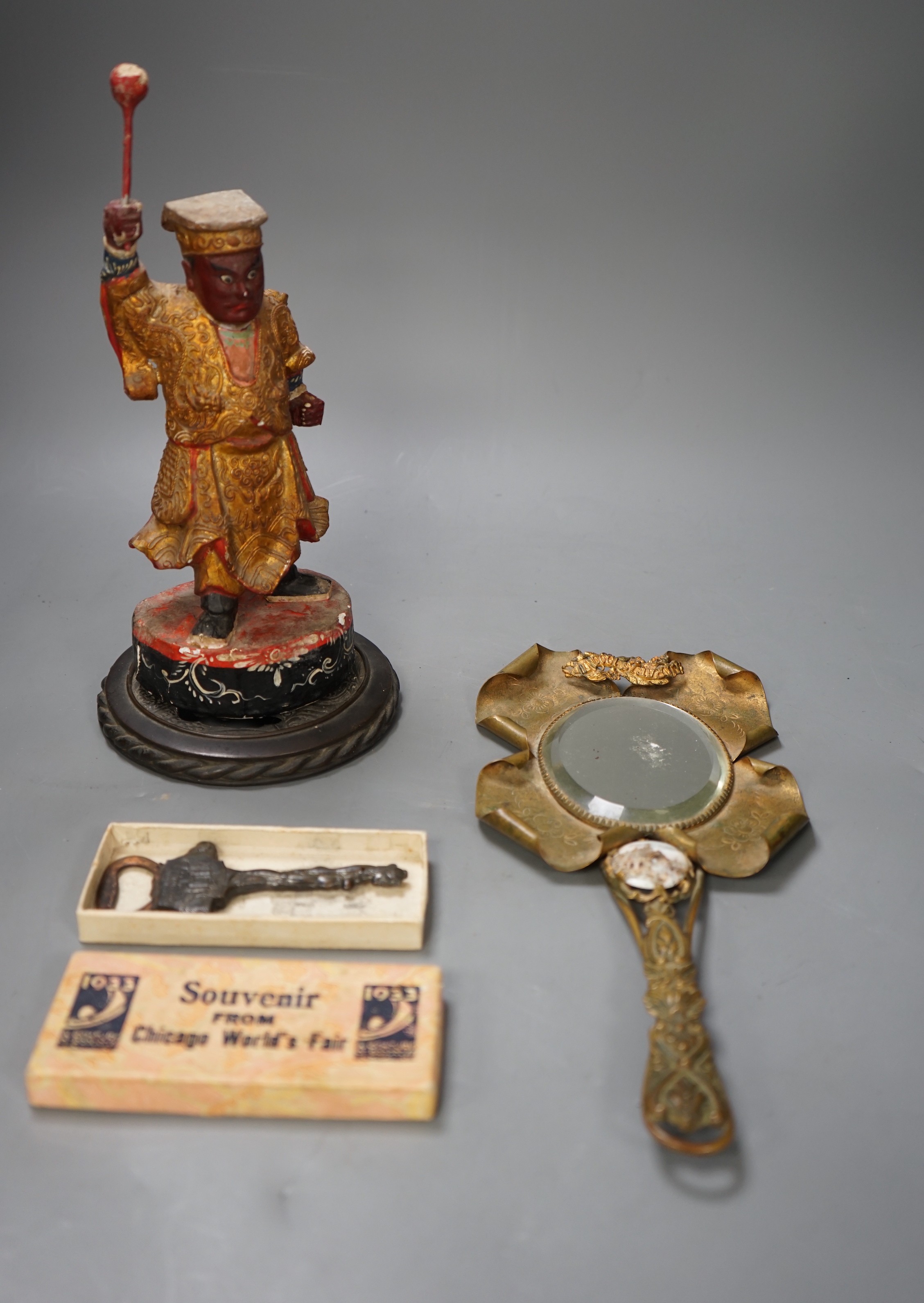 An Oriental carved painted wooden figure, together with an early 20th century 'Chicago World Fair' bottle opener souvenir, and a 1900 Paris exposition mirror with floral and scroll motif (3)